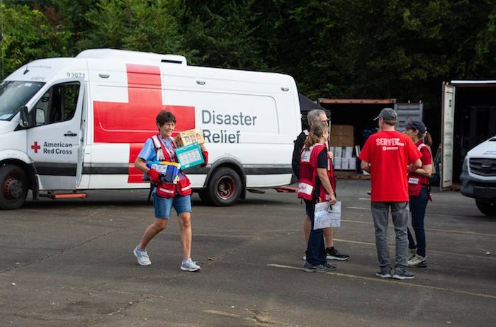 October 2, 2024.  Charlotte, North Carolina
In Charlotte, North Carolina, Red Cross volunteer Betty Beggrow carries supplies to an Emergency Response Vehicle as her fellow volunteers discuss where they will be driving to hand out meals to people impacted by Hurricane Helene.
Photo by Danielle Desnoyers/American Red Cross

