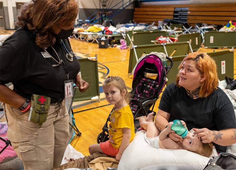 Red Cross volunteer speaking with woman holding baby and child next to her