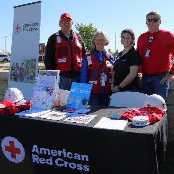 Red Cross volunteers with promotional Red Cross items on table.