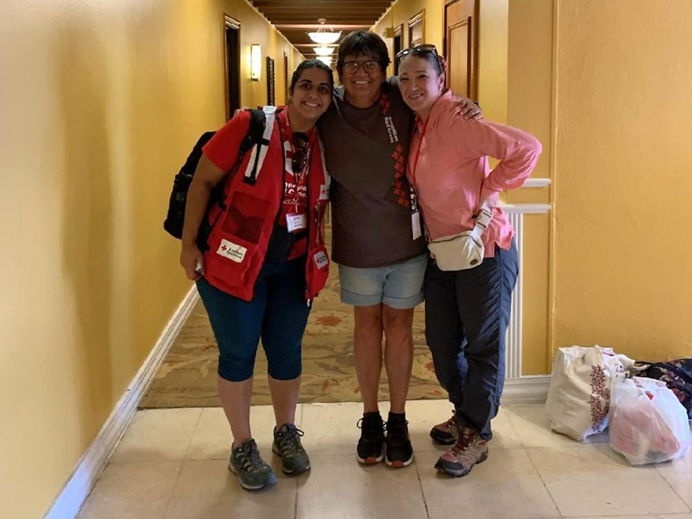Group of three Red Cross volunteers standing in a hallway smiling for camera.