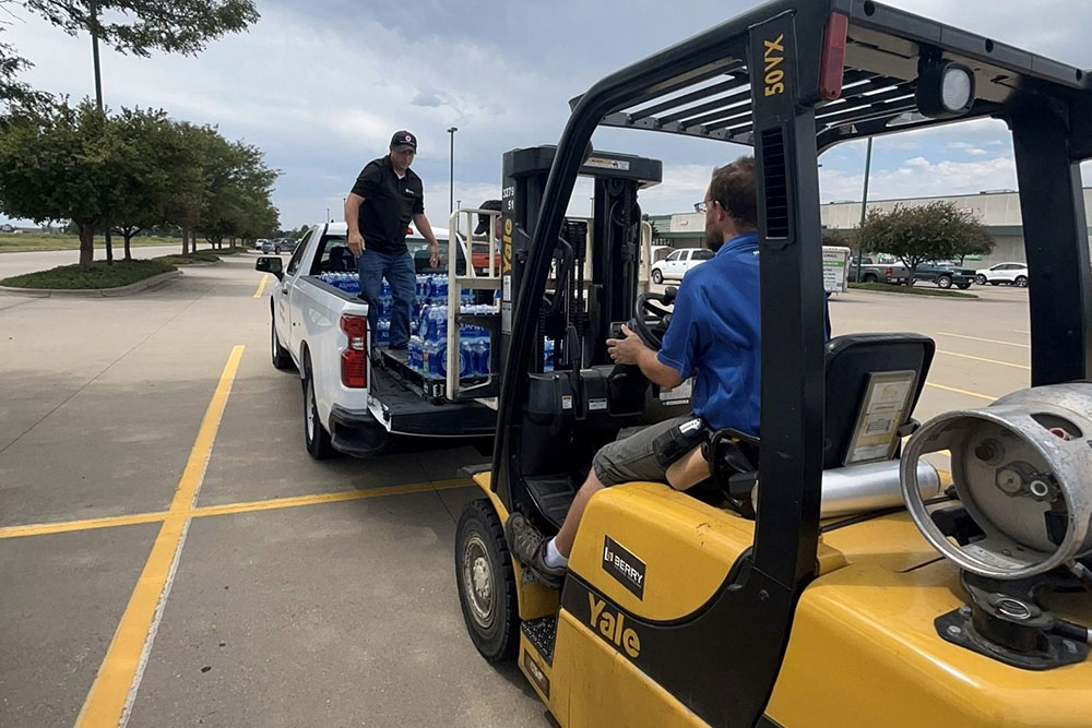 Kyle Lewis works with an employee from Menards home improvement store to transfer a pallet of water from one truck to another with a forklift.