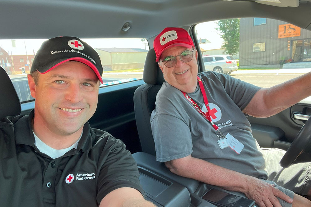 Kyle Lewis and Eric Kohn wearing Red Cross hats and shirts sitting in cab of truck smiling for camera.