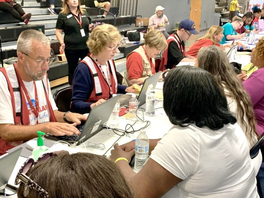 Red Cross volunteers and people sitting at tables getting help