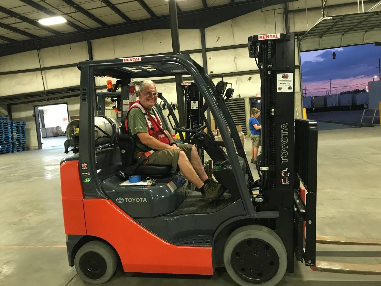 Red Cross volunteer driving a fork lift in a warehouse.