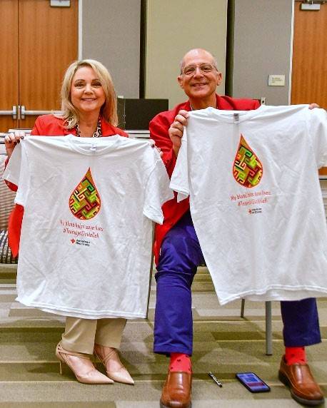 Man and woman holding up t-shirts from donating blood.
