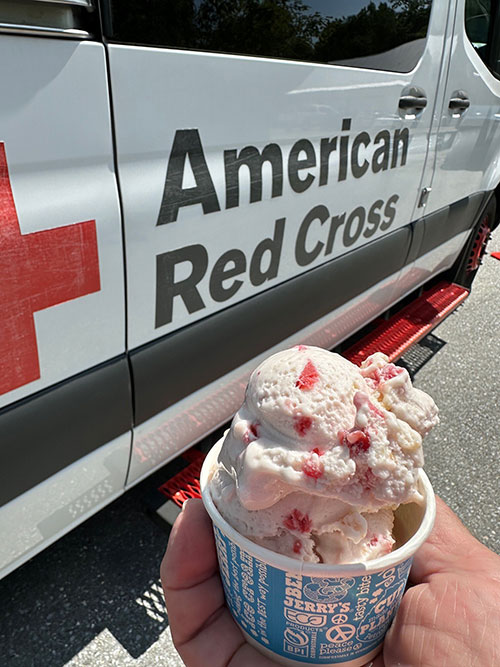 Hand holding a cup of Ben & Jerry's ice cream next to an American Red Cross vehicle.