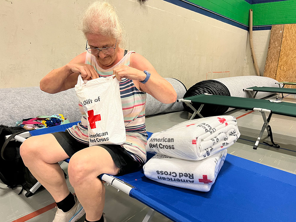 Woman sitting on cot going through Red Cross gift bag.