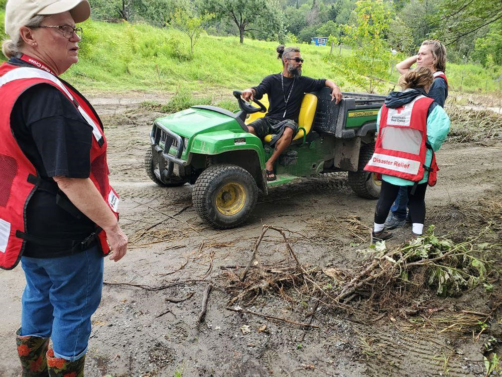 Red Cross volunteers speaking with person on a golf cart driving on a muddy road.