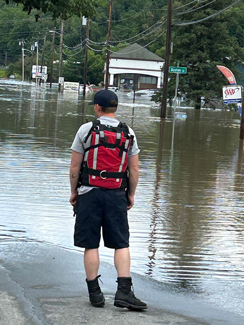 Back of person wearing hat and backpack looking at flooded street.