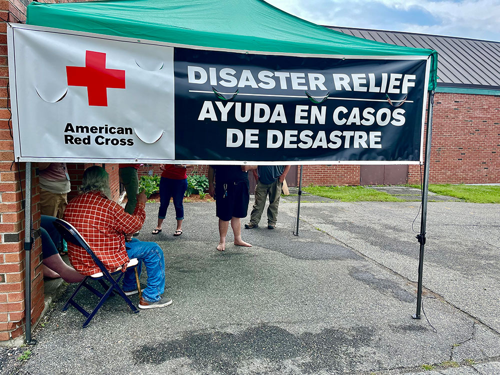People under a canopy with a Red Cross Disaster Relief sign.