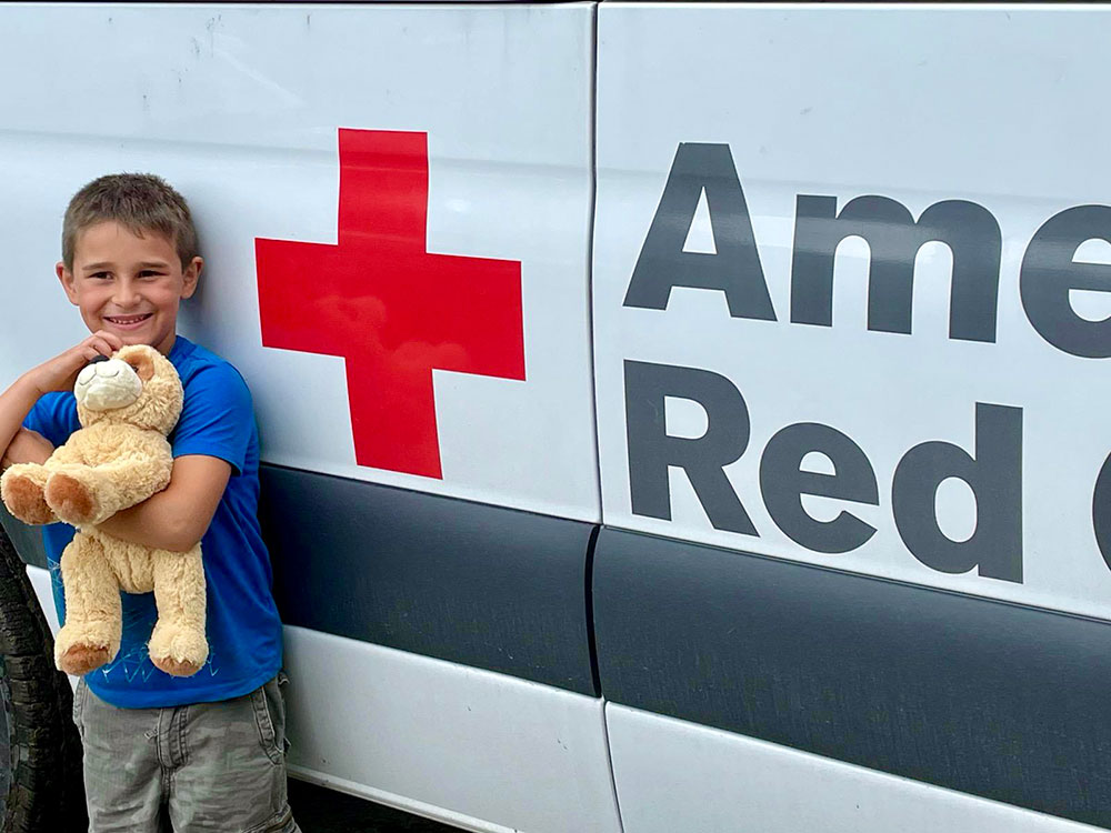 Young boy next to a Red Cross Disaster Relief van holding a stuffed animal.