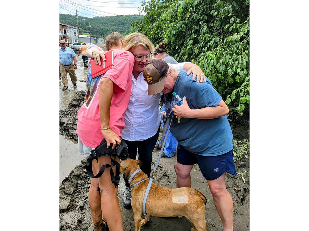 Red Cross volunteer comforting two people and a dog on a leash.