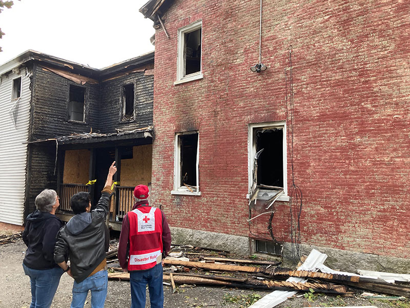 Red Cross volunteer next to a couple of people with one person pointing at burnt building.