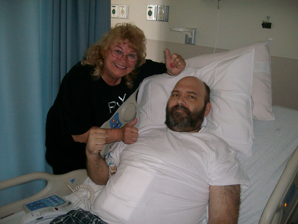 Ray Poulin in hospital bed with woman standing next to him.
