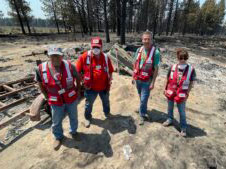 Four American Red Cross volunteers standing on property that has been burned by a forest fire.