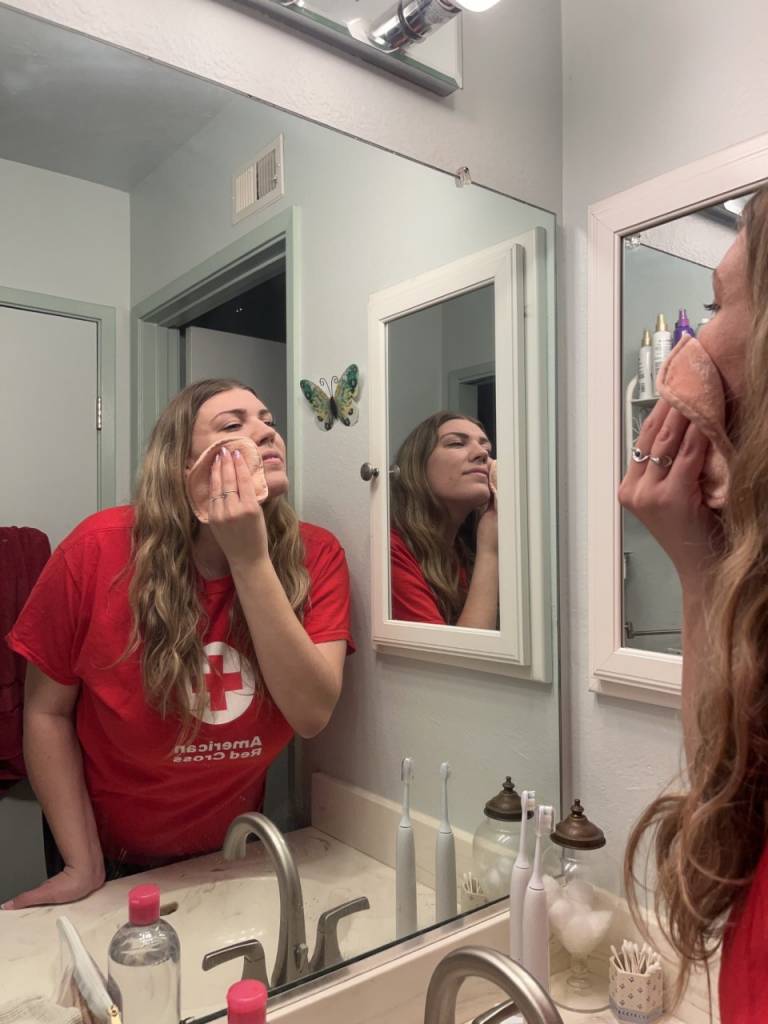 Amy Newell looking mirror while patting face with reusable wipe.