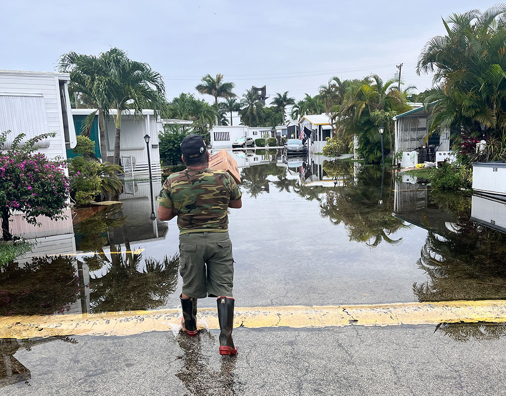 Carlos Alicea carrying box through flooded mobile home park.