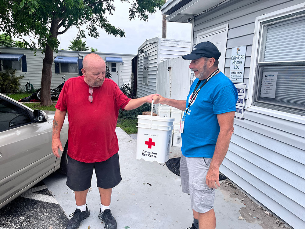 Red Cross volunteer handing a 5 gallon Red Cross bucket to Michael Cary.
