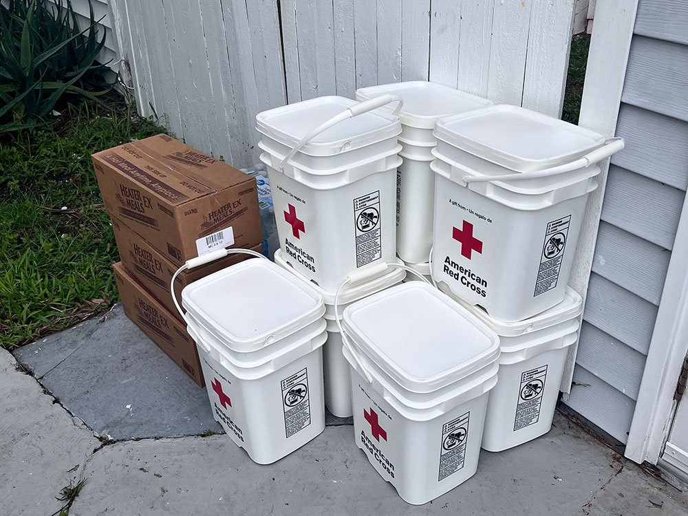 Red Cross 5 gallon buckets and boxes sitting next to a house.