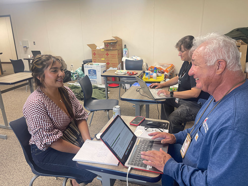 Red Cross volunteer sitting down with woman at table with laptop