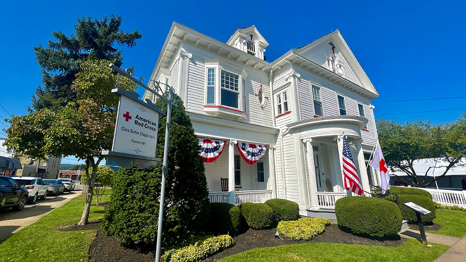 front of Clara Barton Chapter 1 building with USA flag bunting, American flag and Red Cross flag at entrance.