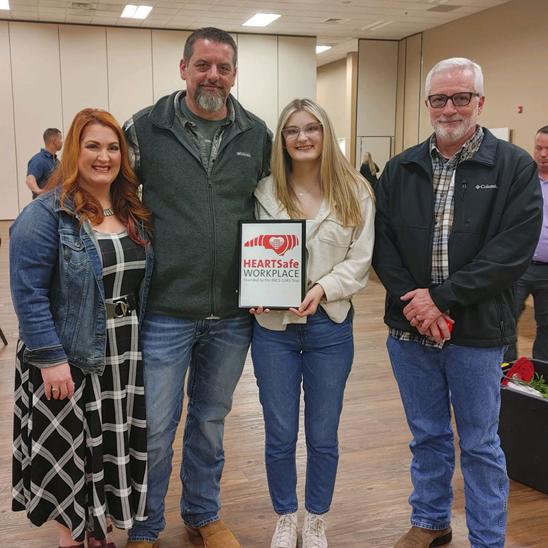 Jason Gibb with wife, daughter and friend. Daughter holding framed HEARTSafe Workplace recognition.