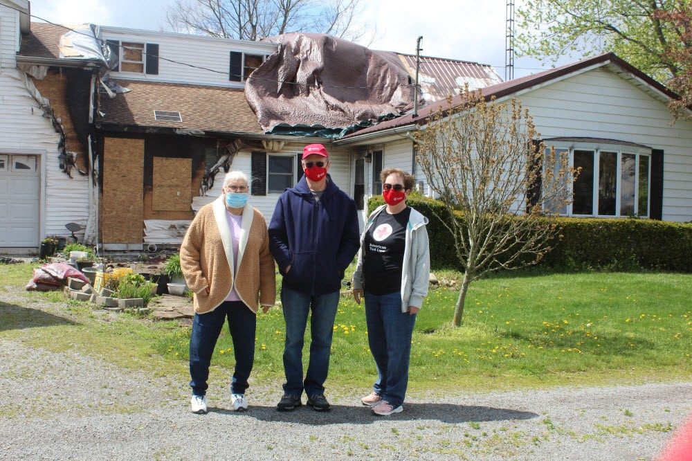 three people wearing mask standing in front of a damaged home