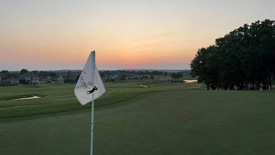 Golf hole cup flag on golf course with houses and trees in the background.