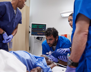 Four medical professionals treating and monitoring a patient in a hospital.