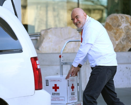 A smiling Red Cross Blood Transportation Specialist picking up a box to deliver.
